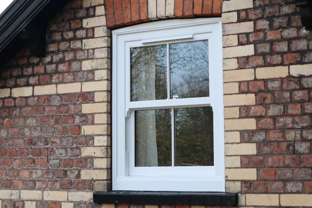 White uPVC sash window with astragal bars and run-through sash horns on a brick home
